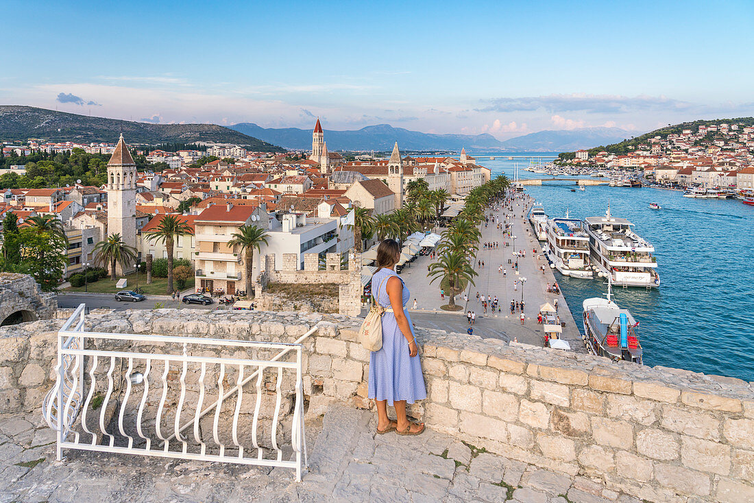 Woman admiring the old town and seafront from Karmelengo castle, in summer. Trogir, Split - Dalmatia county, Croatia.