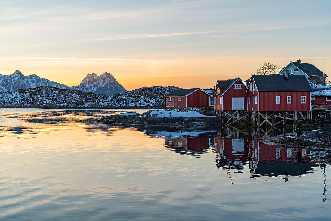 Typische rote Fischerhäuser spiegeln sich im Winter in Morgendämmerung auf dem Meer wider, Svolvaer, Nordland, Region Nordnorwegen, Norwegen