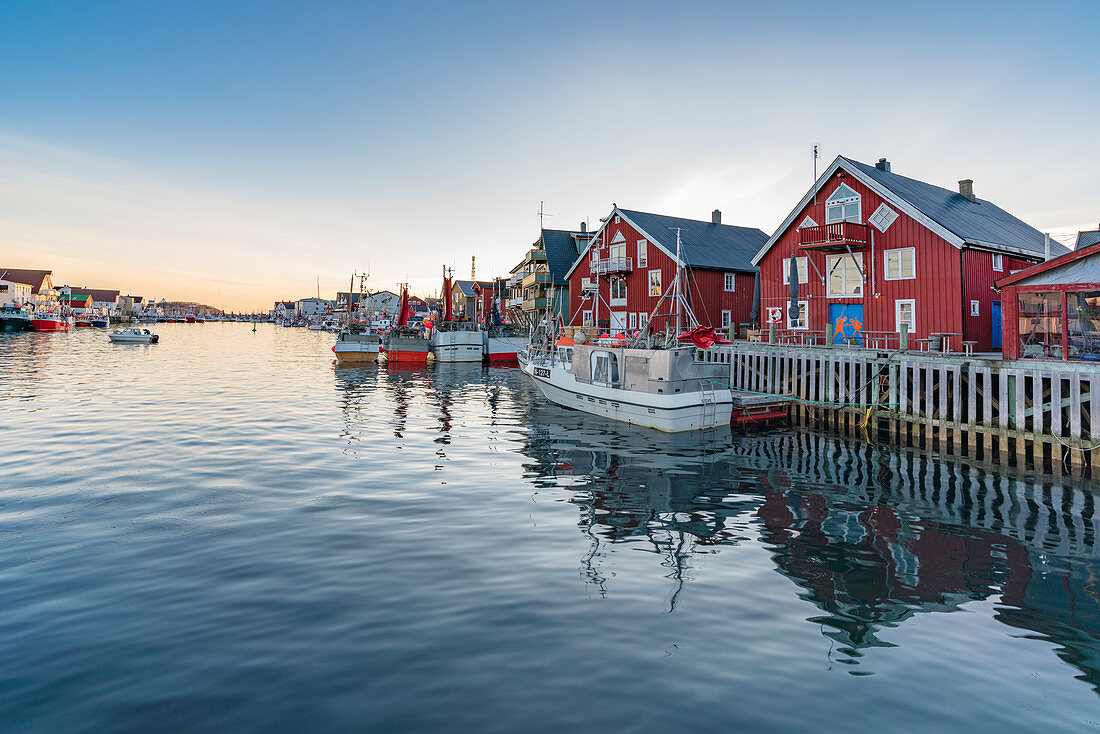 Traditionelle rote Häuser und Fischerboote bei Sonnenuntergang im Winter, Henningsvaer, Nordland, Region Nordnorwegen, Norwegen