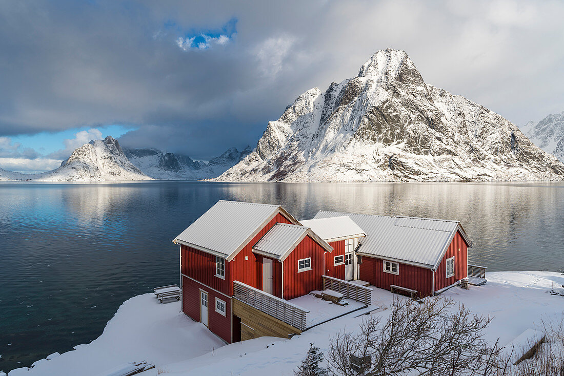 Traditionelle 'Rorbu'-Häuser mit dem Gipfel von Olstinden im Hintergrund im Winter, Reine, Lofoten, Nordland, Nordnorwegen, Norwegen