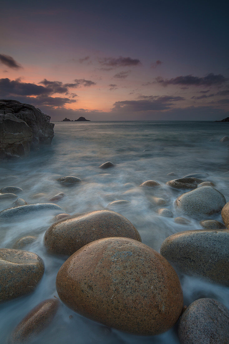 Boulders on Porth Nanven beach looking towards the Brisons at sunset Cot Valley near St Just Cornwall, UK