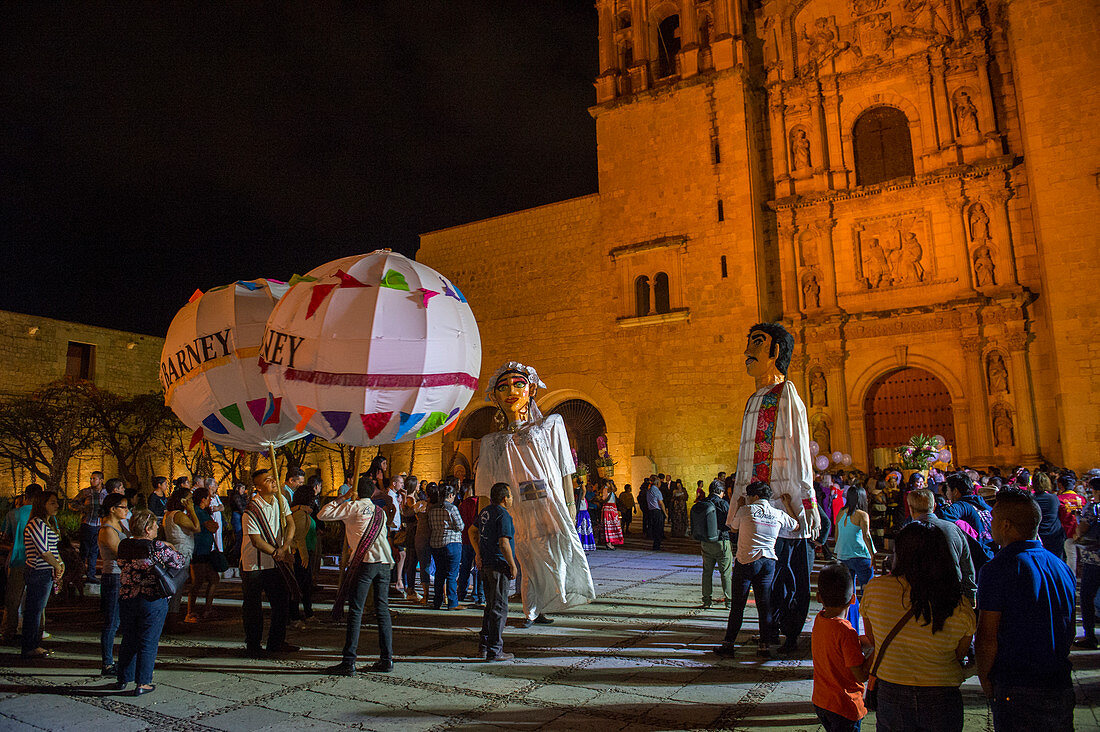 Frauen in einem regionalen Kostüm und riesigen Puppen als Braut und Bräutigam gekleidet während einer Calenda, einer Prozession auf der Plaza Santo Domingo, die eine Hochzeit in der Stadt Oaxaca de Juarez, Oaxaca, Mexiko feiert.