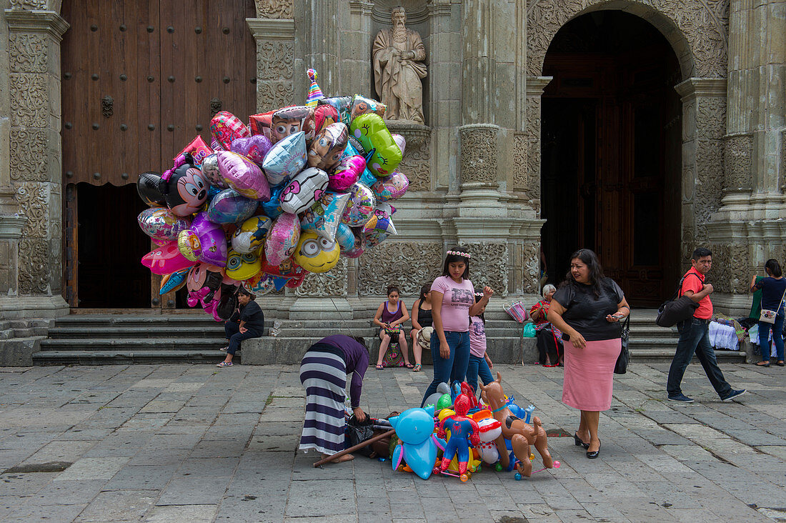 Menschen verkaufen Luftballons auf dem Platz vor der Kathedrale Unserer Lieben Frau von Mariä Himmelfahrt, erbaut in einem neoklassizistischen Stil, in der Stadt Oaxaca de Juarez, Oaxaca, Mexiko.