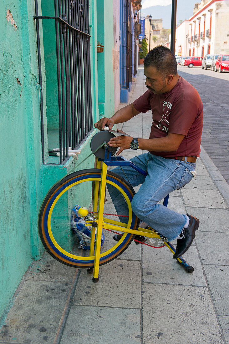 A street scene with a man sharpening knifes in Oaxaca City, Mexico.