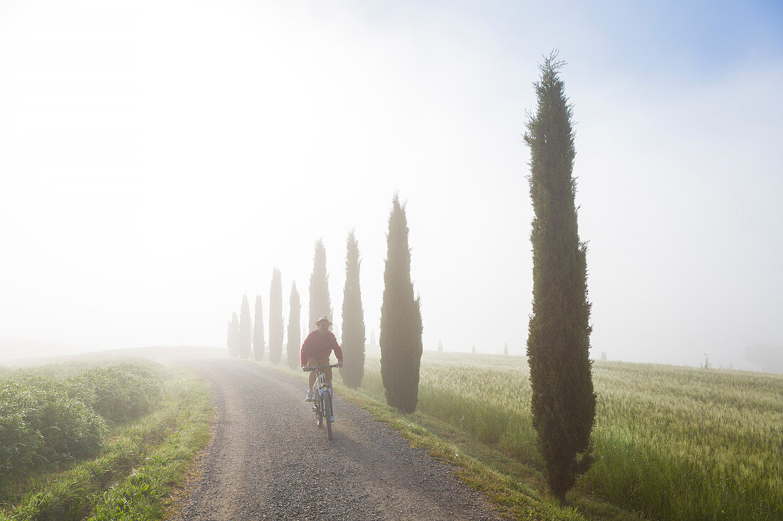 Cyclist on dirt road in early morning in Tuscany Italy. Model released.