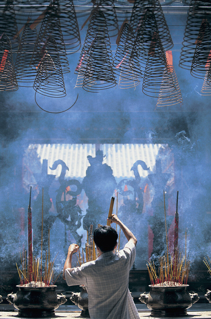 Mann, der Weihrauch in einem asiatischen Heiligtum arrangiert