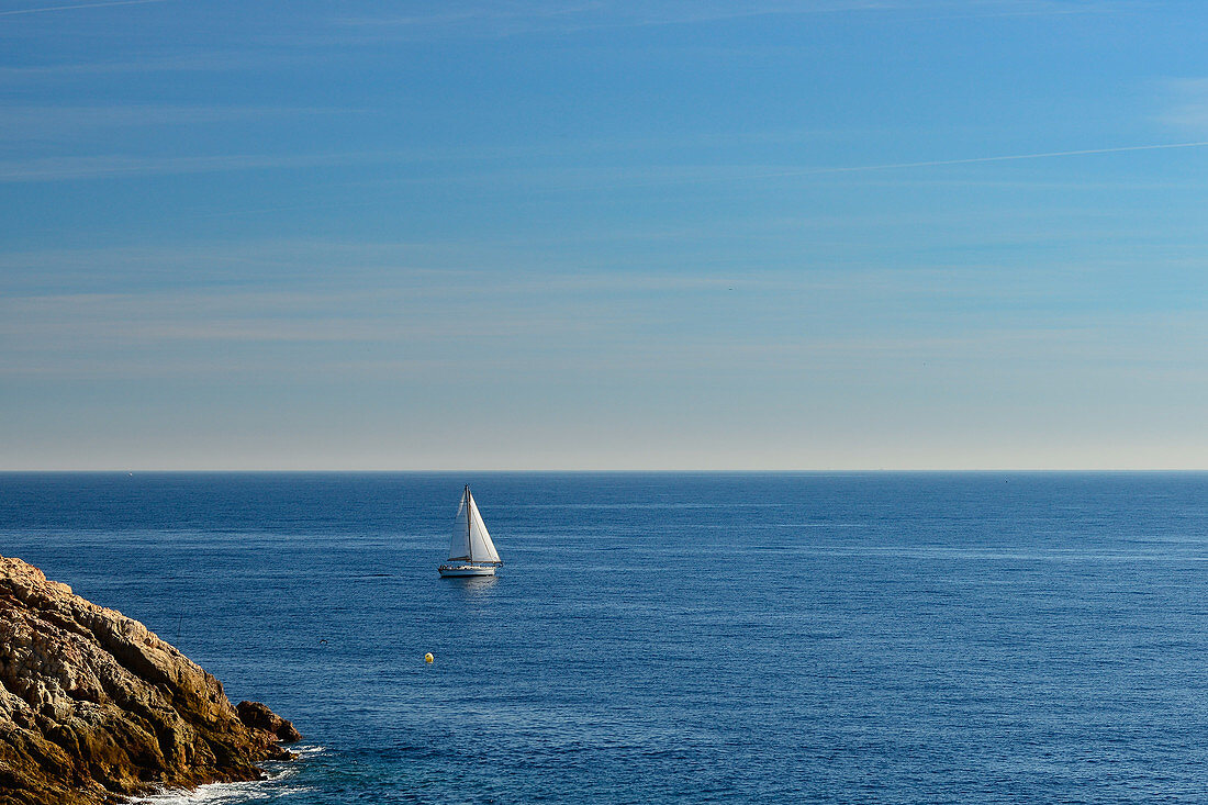 A sailboat near the rocky coast on the Mediterranean Sea, Sant Feliu de Guixols, Catalonia, Spain