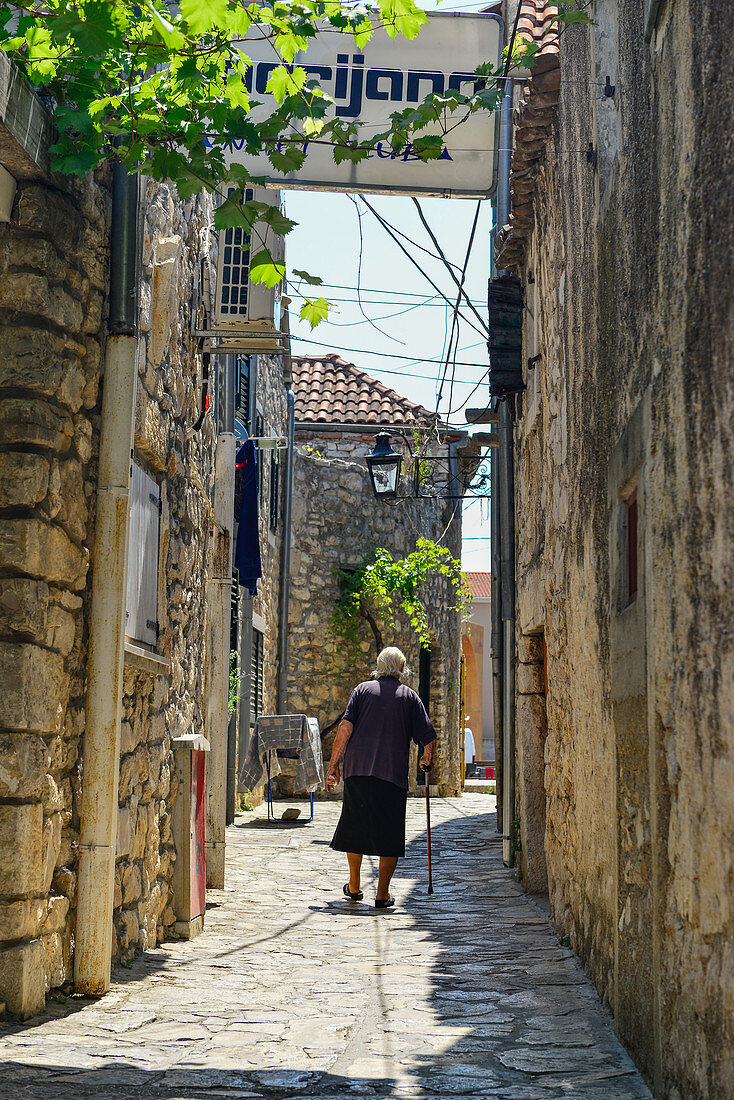 Eine sehr alte Frau geht am Stock durch die engen Gassen, Pakostane, Kroatien