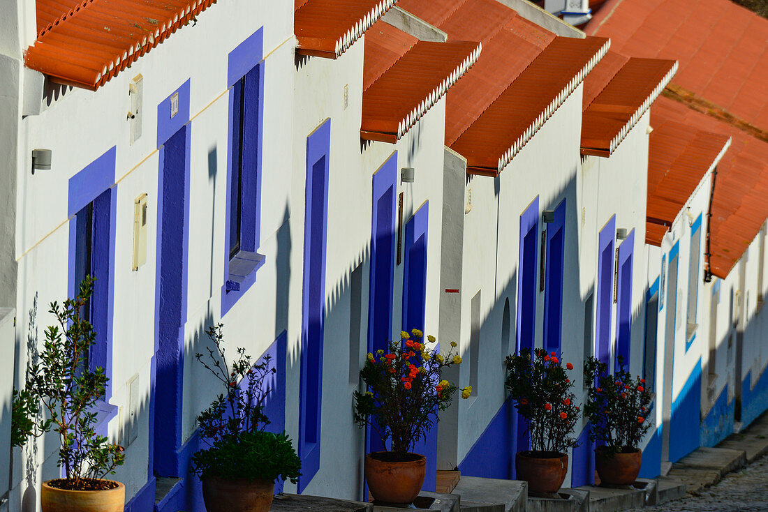 Reihe von Häusern in einer steilen Straße mit blauen Fenstern und roten Dächern, Odeceixe, Algarve, Portugal
