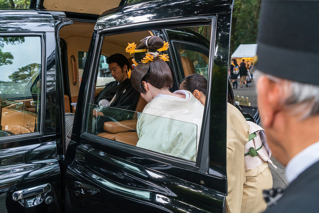 Frau in traditionellem Brautkleid steigt in ein Auto mit Chauffeur, Tokio, Japan