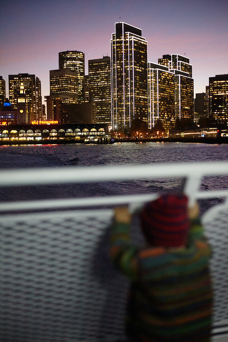 Child on a ferry in front of the sea of lights in San Francisco, California, USA.