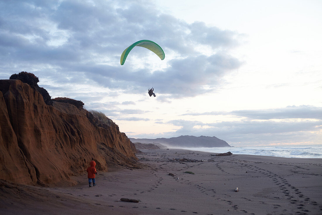 Paraglider pilot with young child at sunset on Point Reyes Beach, California, USA.