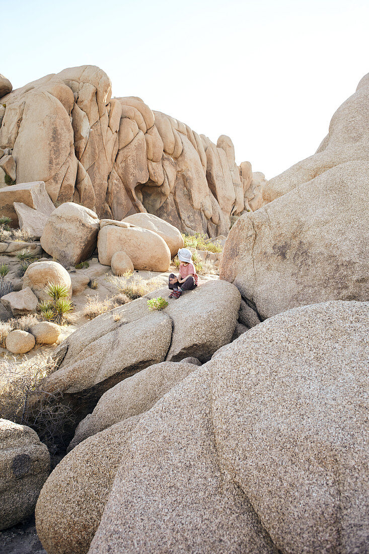 Boy sitting on a rock of Jumbo Rocks in Joshua Tree Park, California, USA.