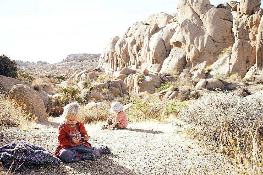 Kinder spielen auf einem Felsen vor der Kulisse der Jumbo Rocks im Joshua Tree Park, Kalifornien, USA
