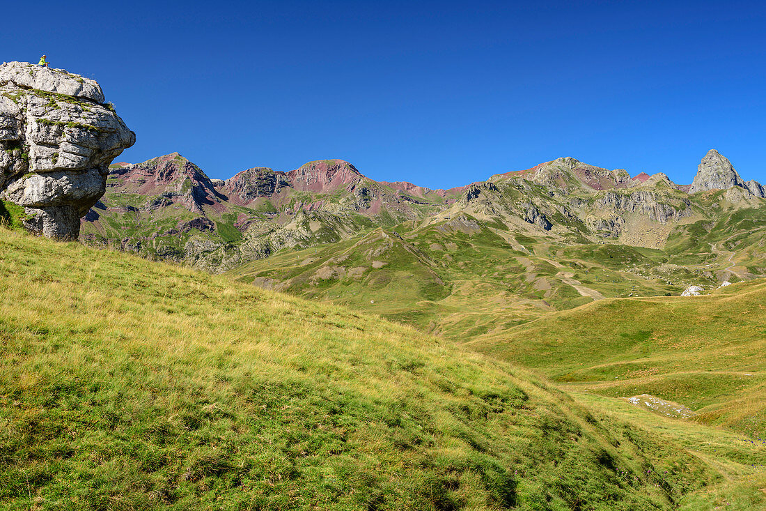Person while hiking sits on rock spur and looks at mountains, at Col de Peyrelue, Pyrenees National Park, Pyrénées-Atlantiques, Pyrenees, France