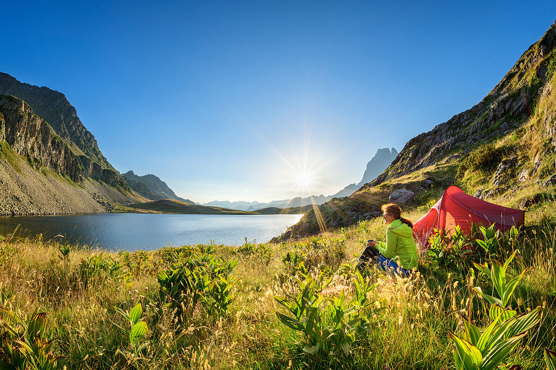 Frau sitzt an Zelt und blickt auf Lac Roumassot und Pic du Midi d´Ossau, Lac Roumassot, Nationalpark Pyrenäen, Pyrénées-Atlantiques, Pyrenäen, Frankreich