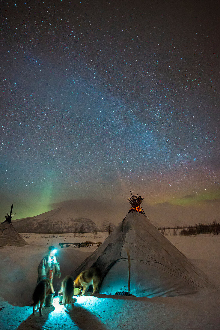 A nenets woman give a food to the dogs under the northern lights at the nomadic reindeer herders camp. Polar Urals, Yamalo-Nenets autonomous okrug, Siberia, Russia