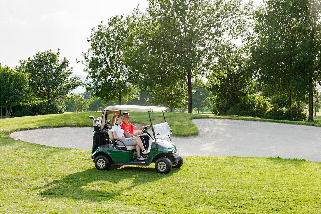 Paar, das auf Buggy auf Golfplatz fährt