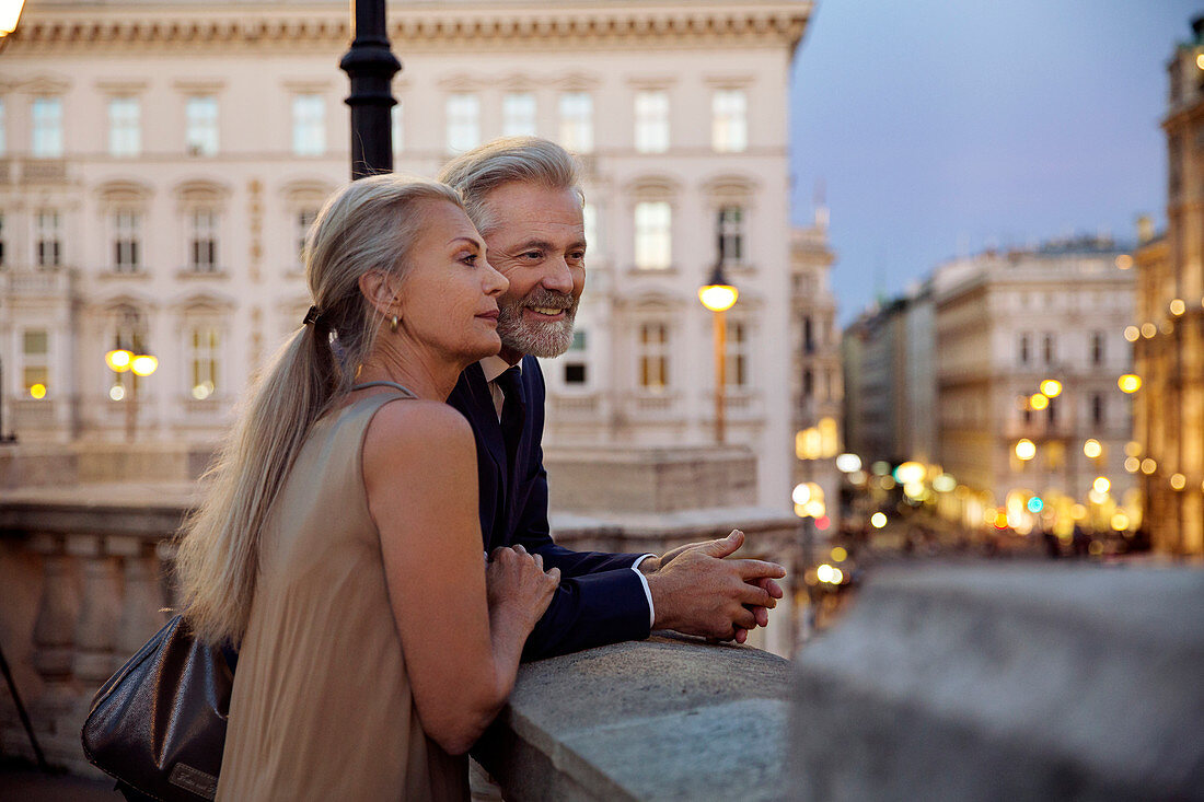 A couple leaning against a balustrade overlooking Vienna during the evening.