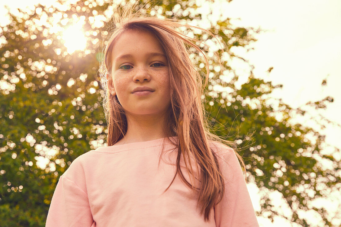 Portrait of smiling girl with long brunette hair standing outdoors, looking at camera.