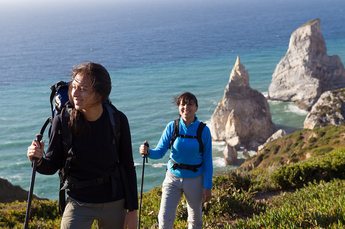 Zwei Frauen mit Rucksäcken und Wanderstöcken entlang der Küste mit Blick auf Seestapel