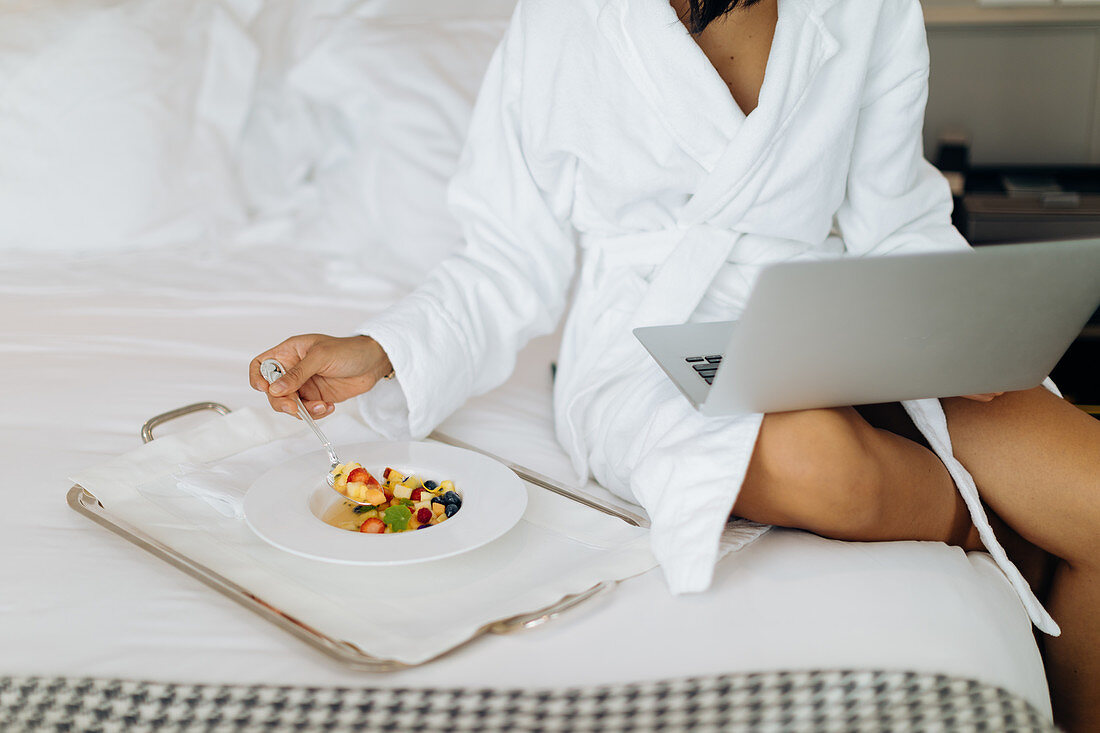 Frau mit Laptop und Frühstück auf dem Bett in der Suite