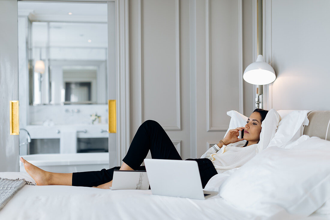 Geschäftsfrau mit Smartphone und Laptop in einer Suite