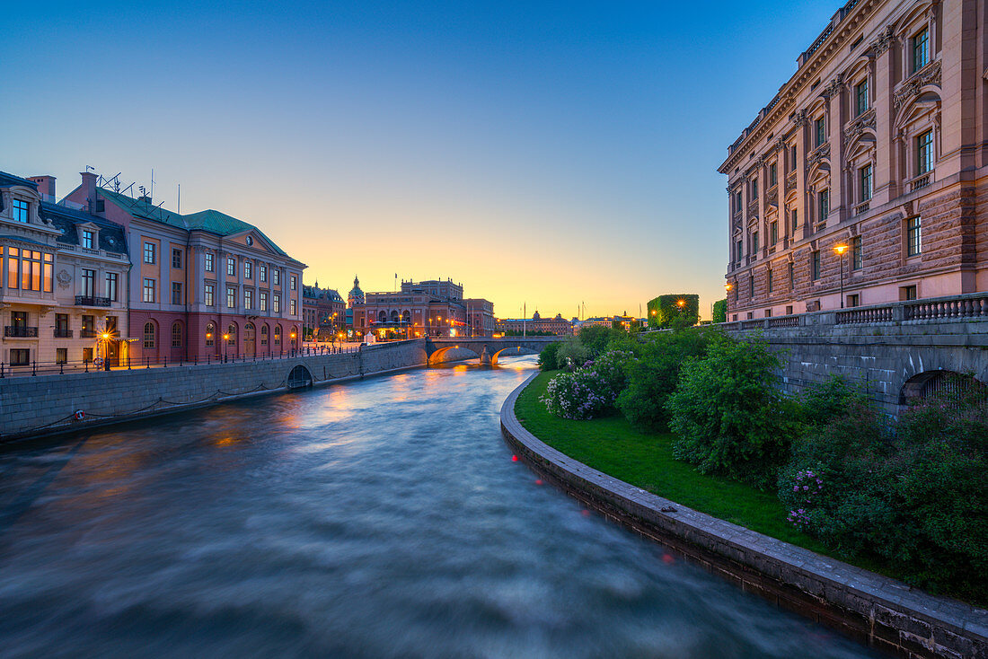 Parlamentsgebäude (Riksdagshuset) und Opernhaus in der Abenddämmerung von der Riksbron-Brücke entlang des Flusses Norrstrom, Stockholm, Schweden