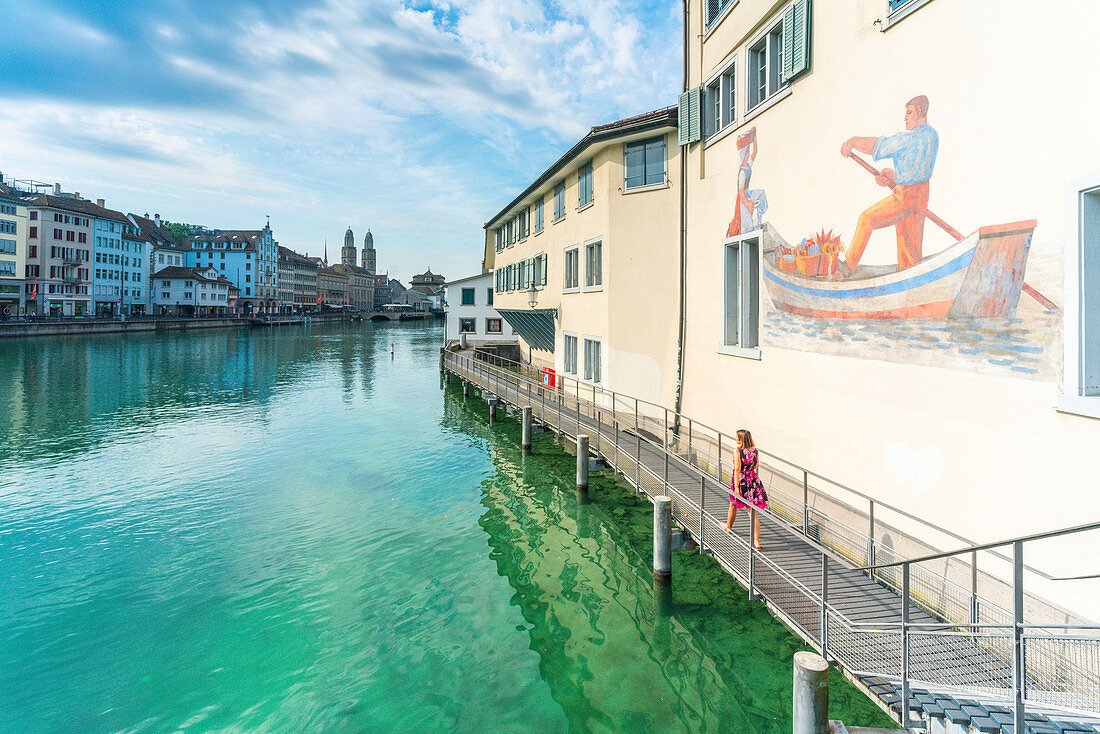 Frau auf erhöhtem Gehweg auf Limmat River neben den gemalten Gebäuden von Lindenhof, Zürich, Schweiz