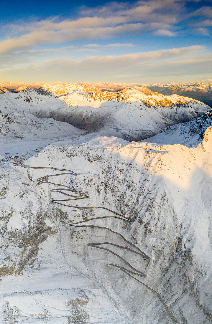 Sonnenaufgang über der kurvenreichen Straße des Stilfserjoch-Passes bedeckt mit Schnee im Herbst, Luftbild, Provinz Bozen, Südtiroler Seite, Italien