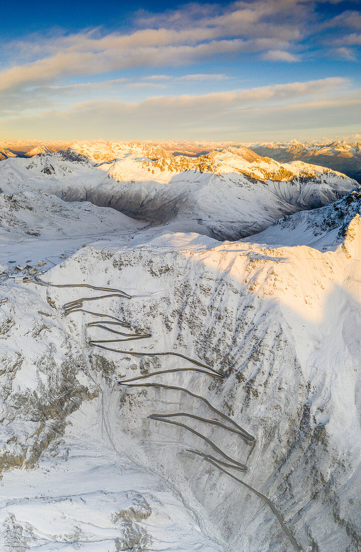 Sunrise over the winding road of Stelvio Pass covered with snow in autumn, aerial view, Bolzano province, South Tyrol side, Italy