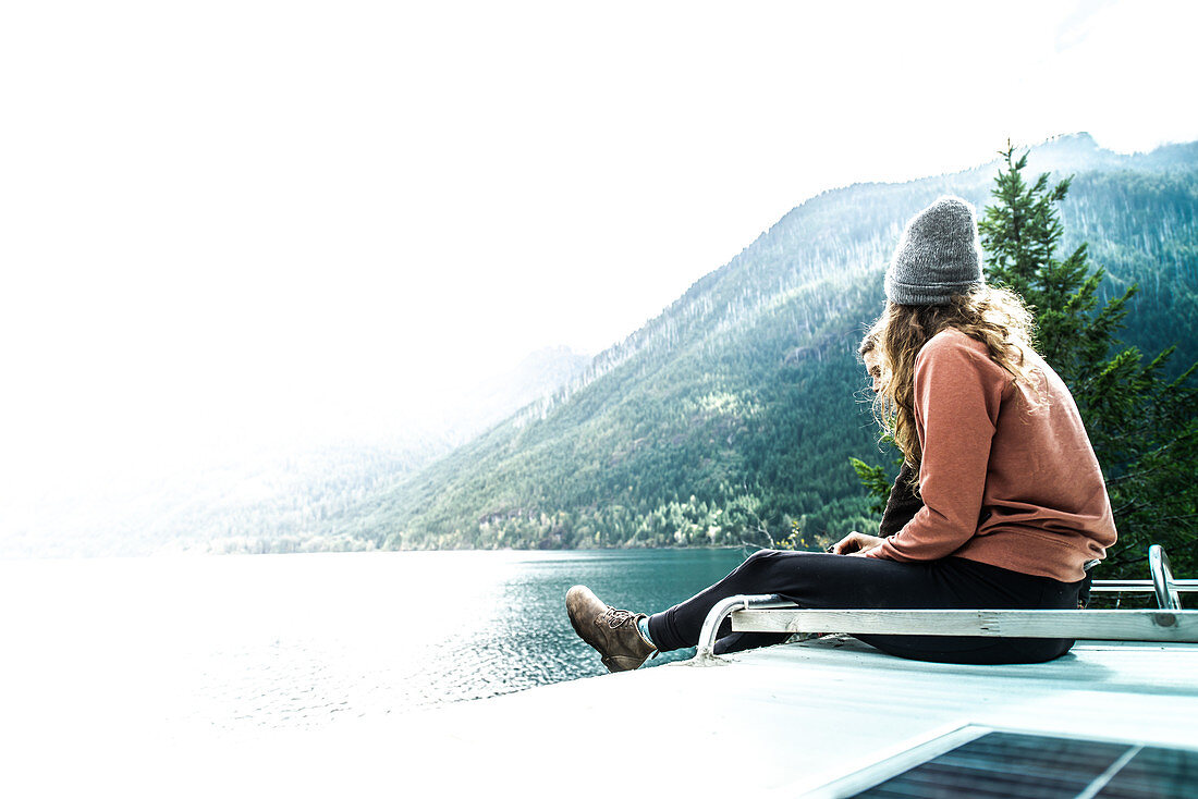 Woman seated on top of campervan overlooking the lake,Cathedral Grove,British Columbia,Canada