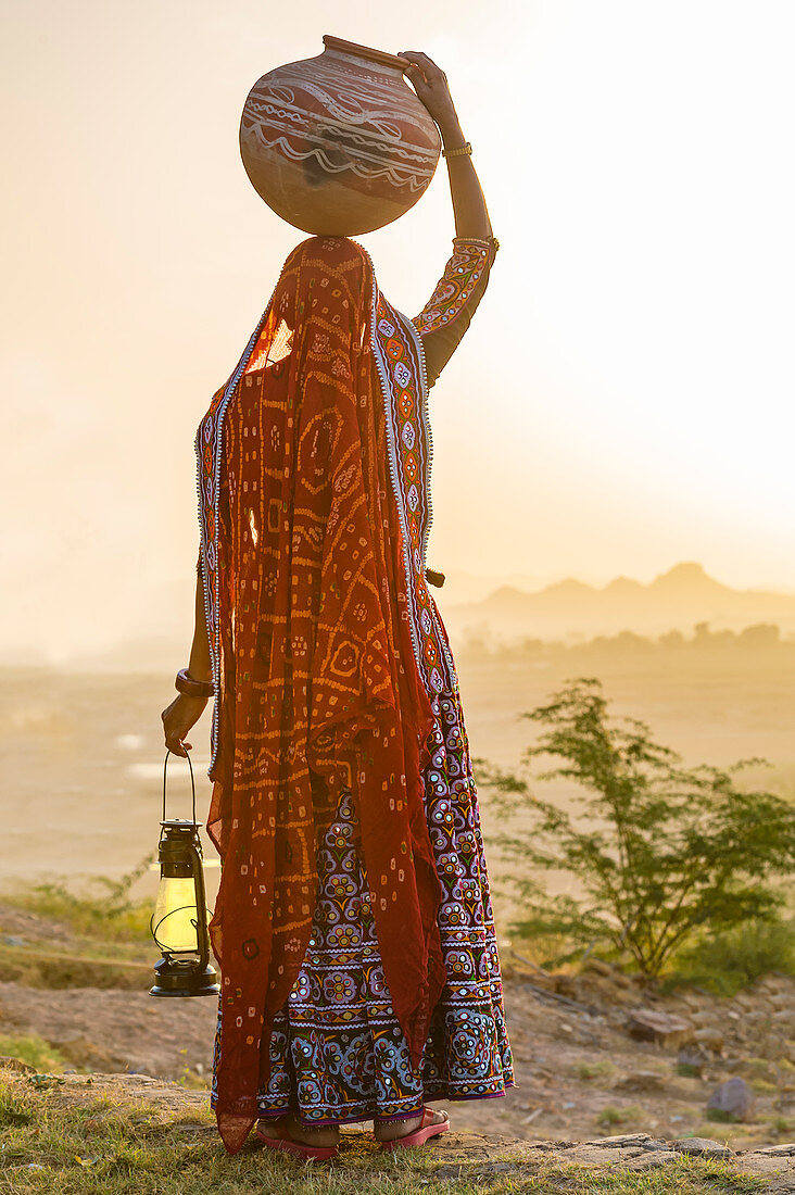 Ahir Frau in traditionellem buntem Stoff, der Wasser in einem Tonkrug auf ihrem Kopf trägt, großer Rann der Kutch-Wüste, Gujarat, Indien, Asien