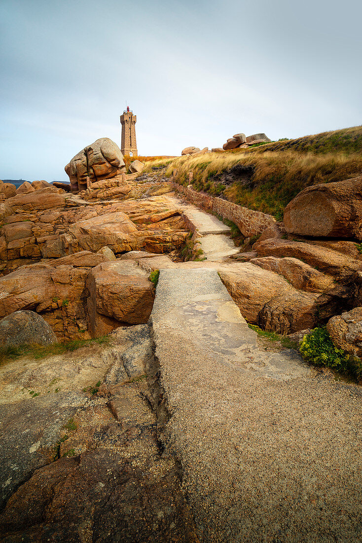 The mean Ruz lighthouse with the red rocks of the Cote de Granit Rose in the foreground, Brittany, France