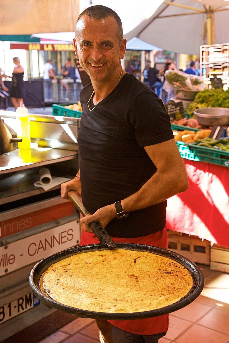 France, Alpes Maritimes, Cannes, Seller of socca, a cake with chickpea flour, on Forville market at the foot of the hill of the Suquet district