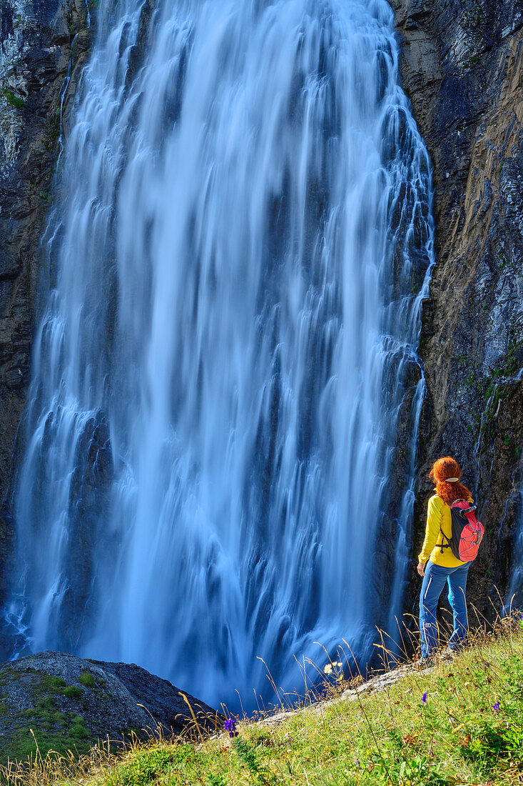Woman hiking stands in meadow and looks at waterfall, Engstligenfall, Adelboden, Bernese Alps, Bern, Switzerland
