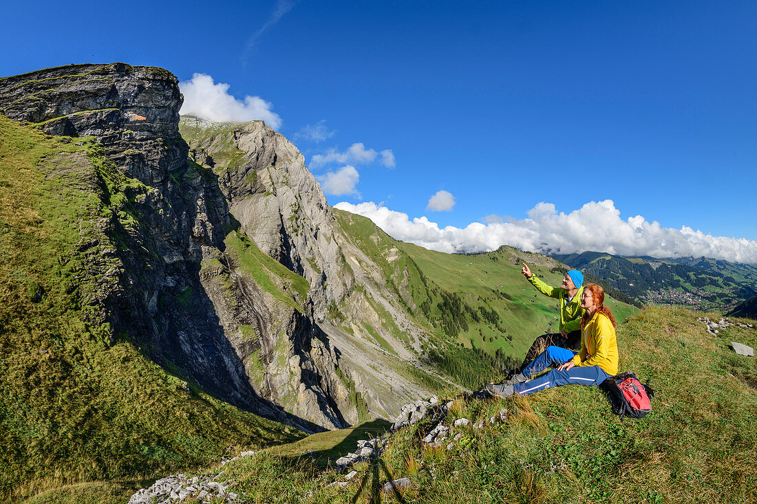 Man and woman while hiking sit on heel and look at mountains, Engstligenalp, Adelboden, Bernese Alps, Bern, Switzerland