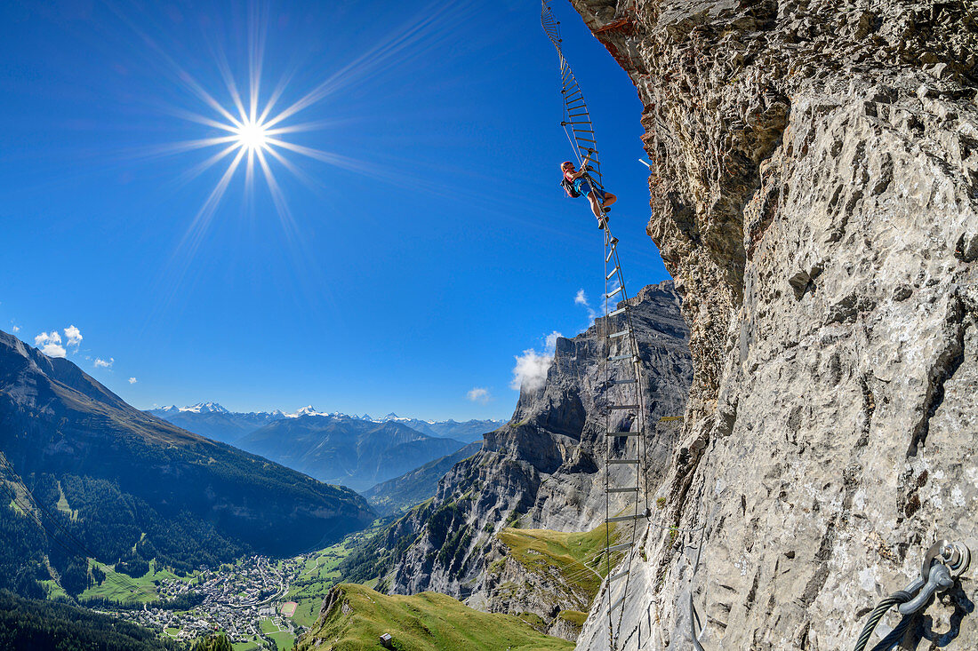 Frau klettert an überhängender Leiter auf Erlebnisklettersteig Gemmi, Leukerbad und Walliser Alpen im Hintergrund, Gemmi, Berner Alpen, Wallis, Schweiz