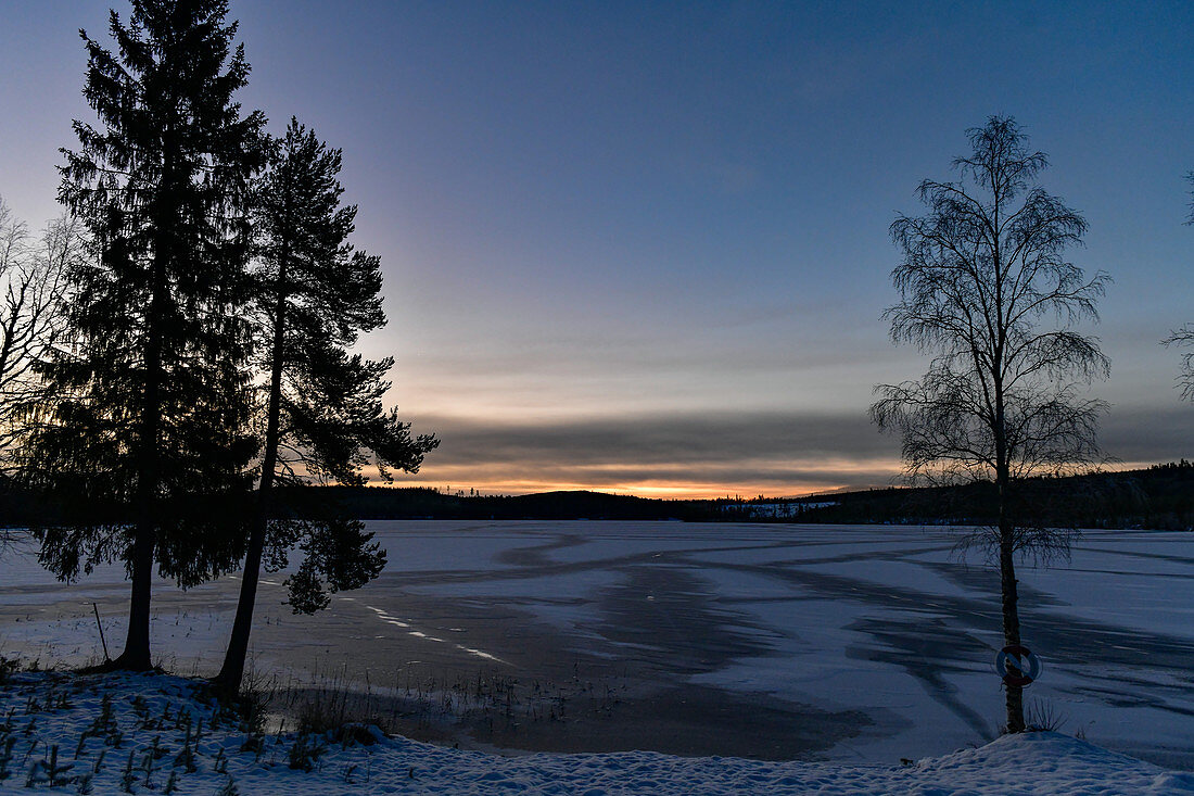 Morgendämmerung über einem vereisten See bei Lycksele, Västerbottens Län, Schweden