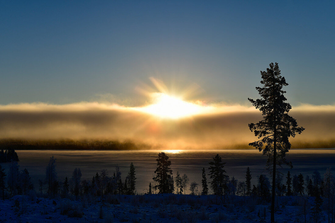 Sonne und Wolken über einem gefrorenen See bei Dorotea, Lappland, Schweden