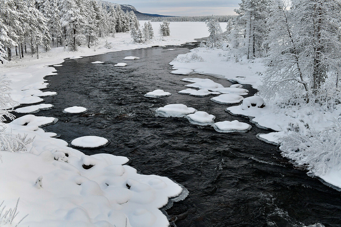 Ein Fluss im Winter umgeben von Eis und Schnee in Lappland, Arjeplog, Schweden