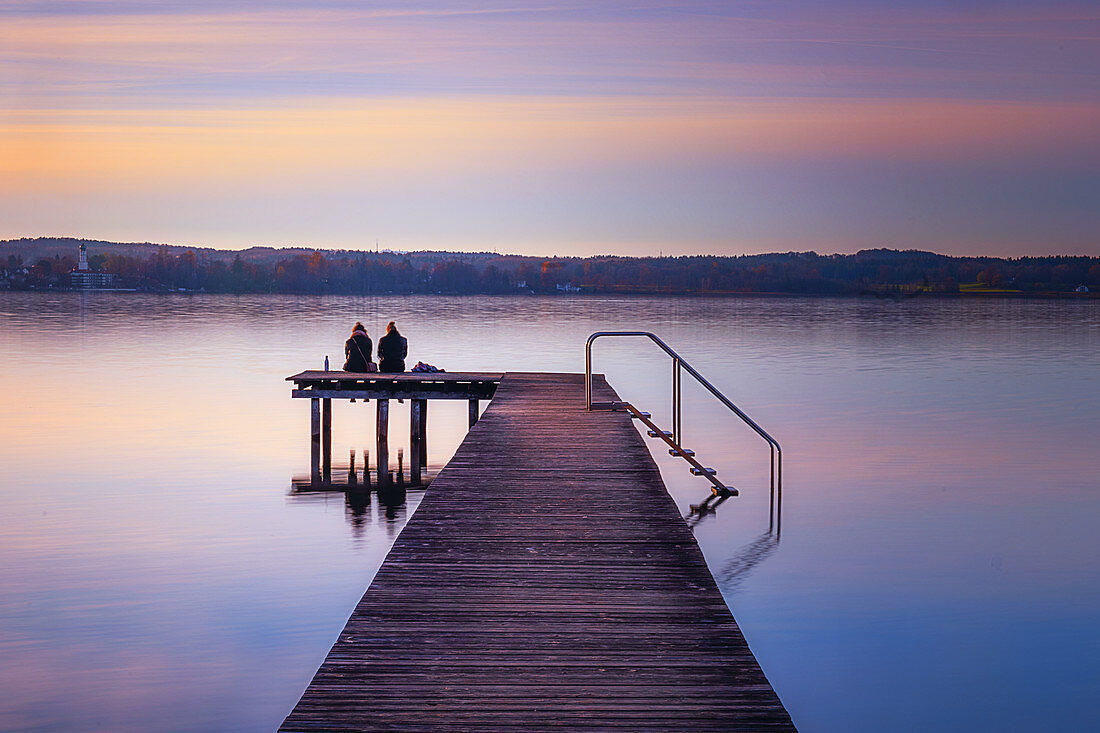 Two women sit on a jetty and look out over Lake Starnberg, Bavaria, Germany