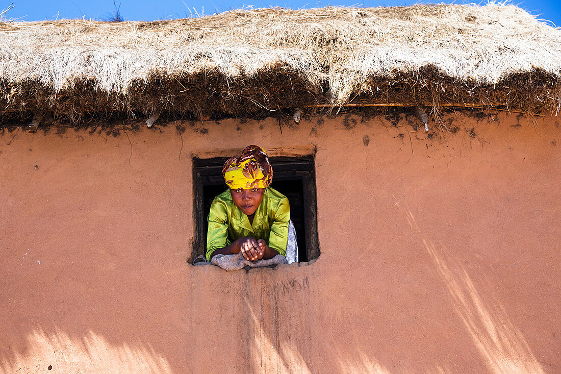 Frau schaut aus dem Fenster, Dorf im Hochland von Madagaskar, Afrika