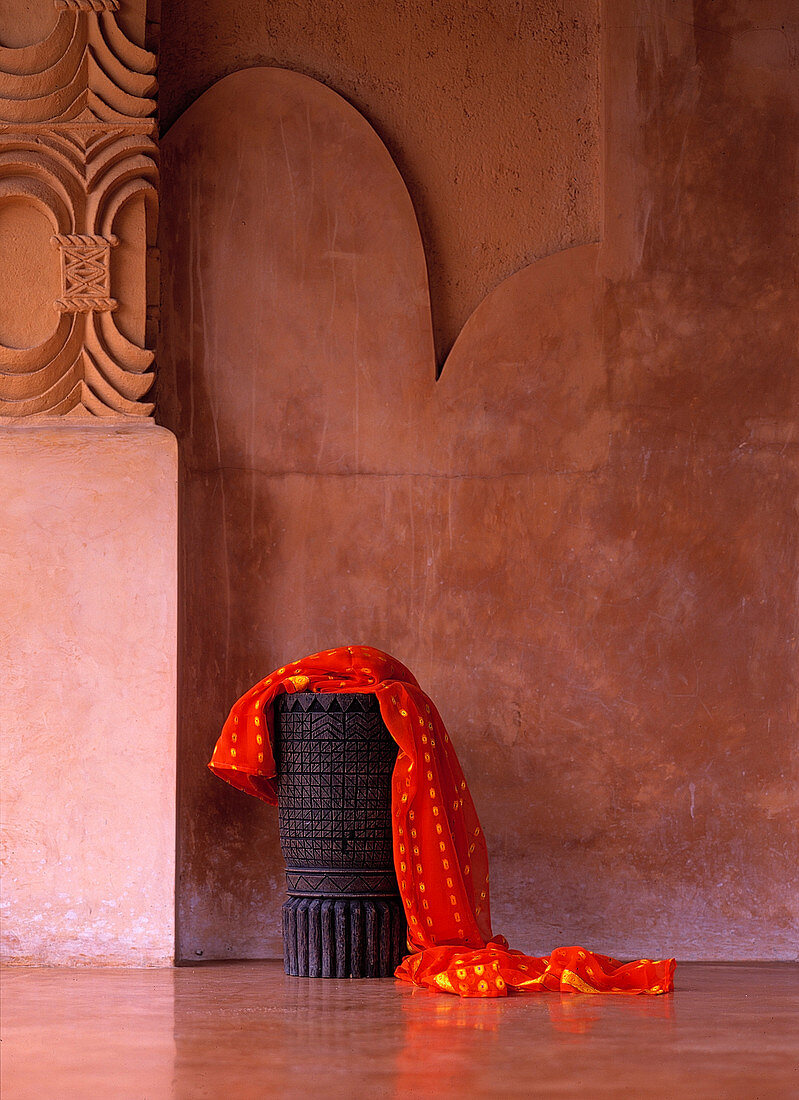 Sarong über einem hölzernen, geschnitzten Hocker, vor einer polierten, verzierten Wand, Lombok, Indonesien.