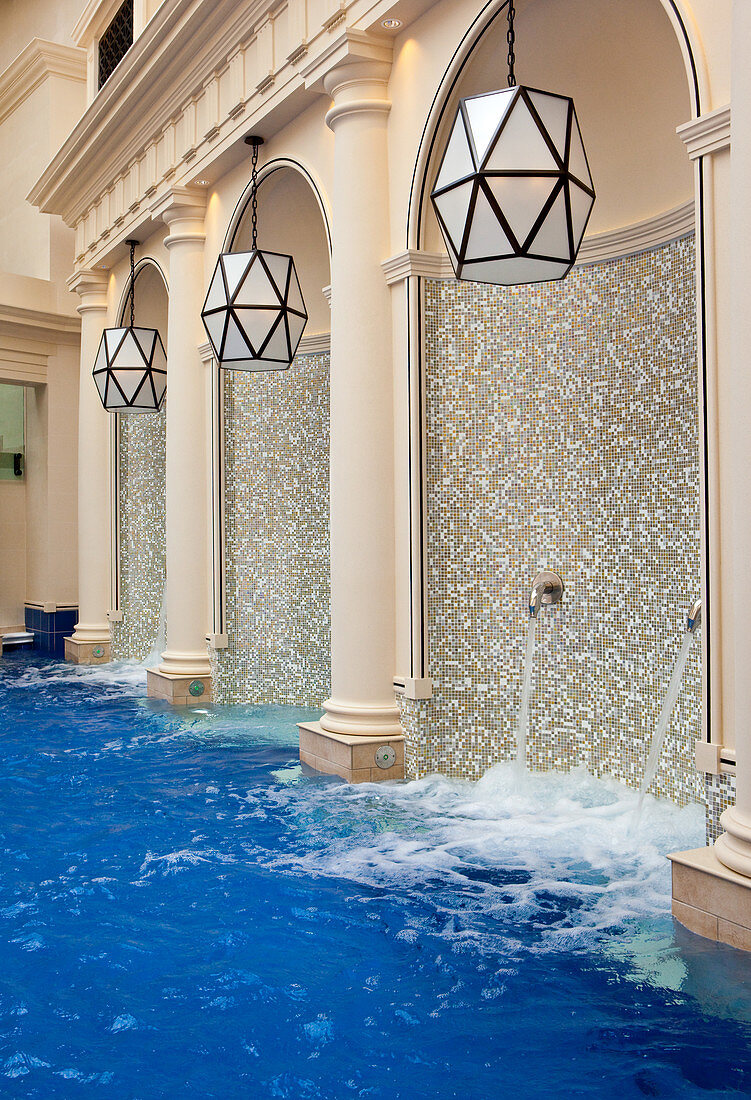 Wasserstrahlen fließen in einen mit Mosaiken und Säulen verzierten Innenpool. Bath, Vereinigtes Königreich