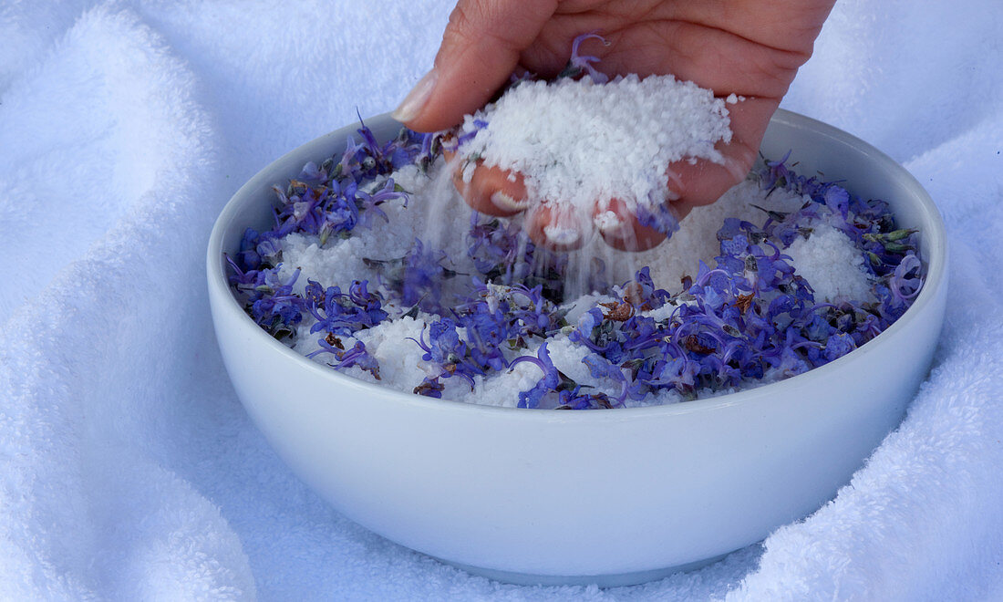 A woman´s hand in a bowl with sea-salt and blue flowers. Algarve, Portugal.