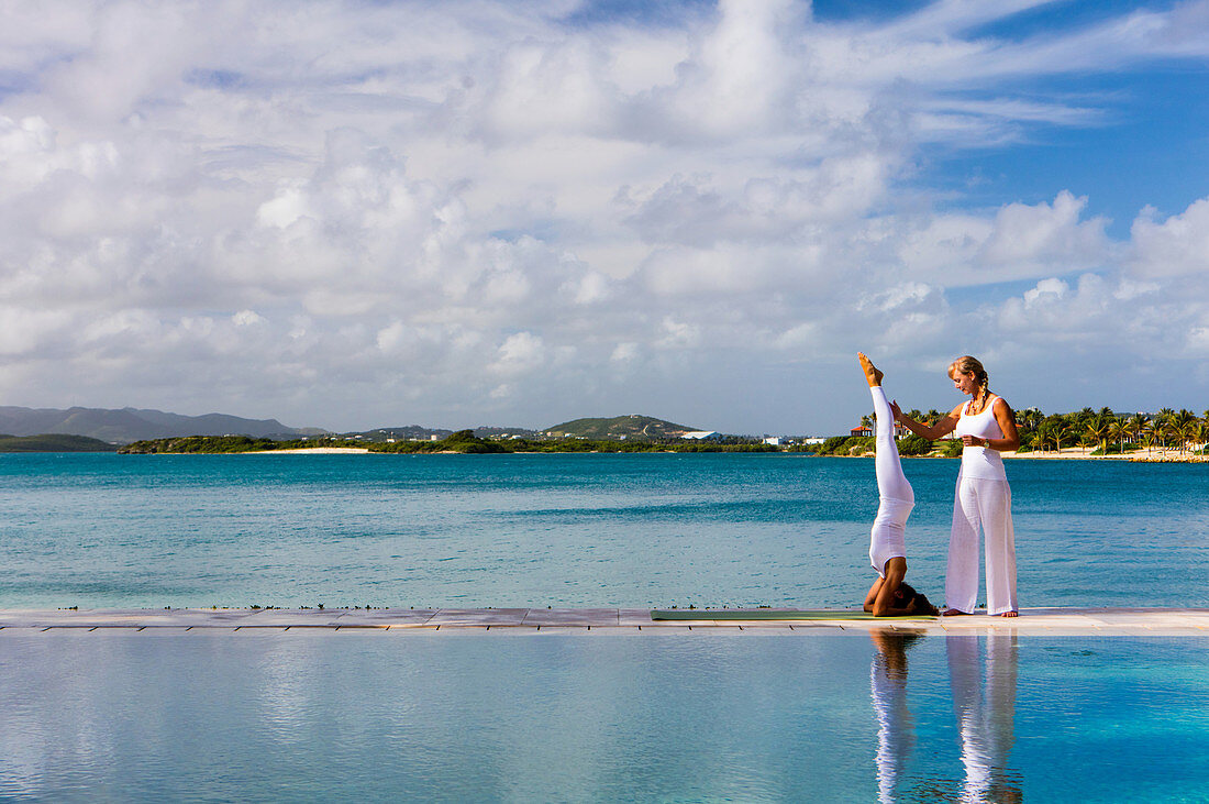 Ein Yogalehrer gibt den Gästen Anweisungen auf einer Plattform zwischen einem Pool und dem Meer. Antigua, Westindische Inseln.