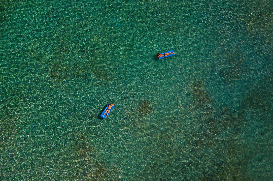 Zwei Frauen, die auf Luftmatratzen schwimmen, schweben im klaren blauen Meer. Luftaufnahme, Britische Jungferninseln.