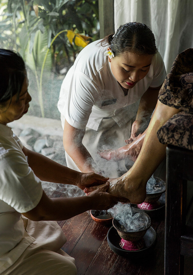 Balinesischer Therapeut, der ein Fußritual mit Rauch von heilenden Hackschnitzeln und Weihrauch durchführt, Bali, Indonesien.