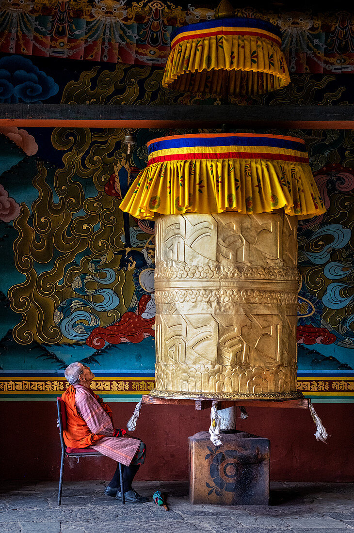 Portrait of elderly Buddhist monk turning prayer wheel, Punakha Dzong, Bhutan, Asia